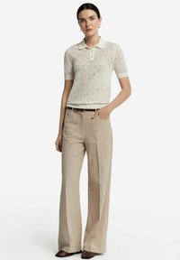 Spets polo-skjorta i off-white med diamantmönster, matchad med ljusbeiga vida byxor och bruna texturerade skor.