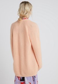 Peach-colored, oversized knitted sweater with a soft texture and long sleeves, featuring a round neckline and relaxed fit.