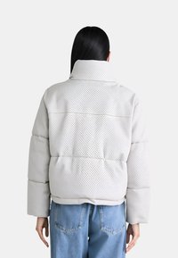 Giubbotto puffo grigio chiaro, caratterizzato da una texture trapuntata e un colletto alto. Abbinato a jeans in denim blu larghi.