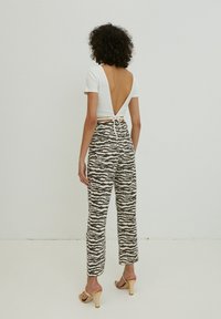 Weißes, geripptes Cropped Top mit offener Rückseite und Bindedetail; gemusterte beige und schwarze Palazzo-Hosen mit wavy Linien; nuda Absatzsandalen.