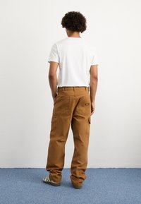 Ruskeat cargo-housut, joissa on useita taskuja, suora malli ja kestävä kangas. Yhdistettynä yksinkertaiseen valkoiseen t-paitaan ja raidallisiin jalkineisiin.