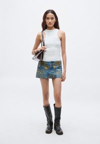 Τζιν μίνι φούστα με μεταλλικά τρουκς σε γεωμετρικά σχέδια, συνδυασμένη με εφαρμοστή λευκή αμάνικη μπλούζα και μαύρες δερμάτινες μπότες μέχρι το γόνατο.