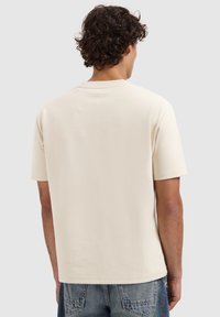 Korte mouwen, crèmekleurig t-shirt van zachte stof met een ronde halslijn en rechte snit, met een klein naaddedetail op de rug.