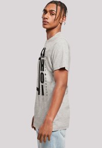 Graues Baumwoll-T-Shirt mit Rundhalsausschnitt, kurzen Ärmeln und fettem schwarzen vertikalen Grafiktext auf der Vorderseite. Lässige Passform.