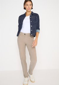 Džínová bunda v tmavě modré barvě, přiléhavá, se dvěma náprsními kapsami a stříbrnými knoflíky. Světlé béžové kalhoty s předními kapsami, na míru, s hladkou texturou.