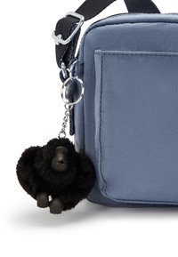 Portachiavi di gorilla in peluche nero attaccato a una borsa di tessuto blu, con finitura liscia, forma rettangolare e cerniera rinforzata.
