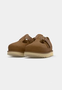 Bruine suède schoenen met een afgeronde neus, met uitsnijdingen en een verstelbare band. Zachte, gestructureerde bovenkant en een contrasterende witte outsole.