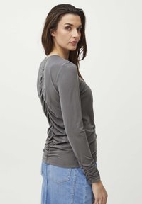Grå langærmet bluse med sammensyning langs bagsømmen, parret med en denimnederdel, der viser en glat, tekstureret stof.