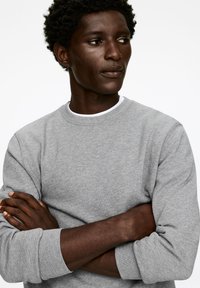 Gray crew neck sweatshirt made of soft cotton blend, featuring long sleeves with ribbed cuffs. Smooth texture, minimalistic design.