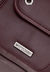 Bordo torebka z syntetycznej skóry z metalową tabliczką z logo, srebrnym oczkiem i precyzyjnym przeszyciem wzdłuż krawędzi.