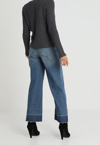 Donkergrijs gebreid trui met textuur, lichtblauwe denim jeans met wijde pijpen en franjes aan de zoom, en zwarte hoge hakken enkelboots.
