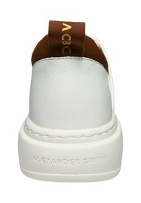 Sneaker bianca in pelle con un accento marrone sul tallone, dotata di una linguetta con marchio e una suola testurizzata, che mostra lettere in rilievo.