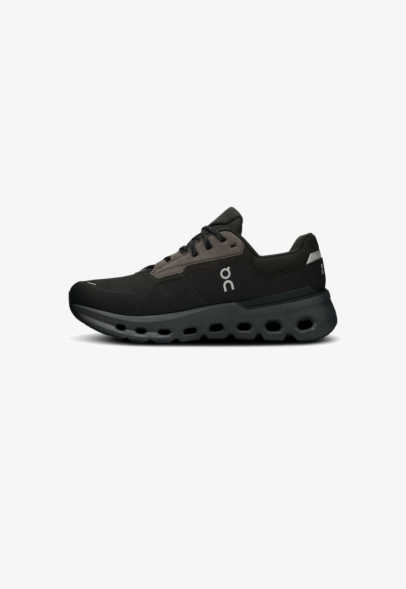 Chaussures de sport noires avec une tige texturée, présentant un accent gris, des lacets ronds et une semelle flexible avec des découpes hexagonales.