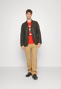 Dark brown jacket with two chest pockets, red graphic t-shirt, beige trousers, and brown shoes; smooth texture, casual fit.