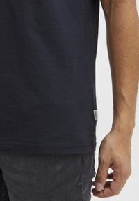 Tricou din bumbac bleumarin cu mâneci scurte, dotat cu o etichetă pe lateral și o textură moale și netedă, asortat cu blugi distresați de culoare gri închis.