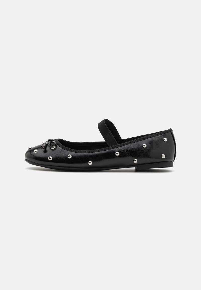 Zapato plano de cuero negro con punta redonda, tachuelas decorativas plateadas y una correa elástica. Presenta una textura lisa y un tacón bajo.