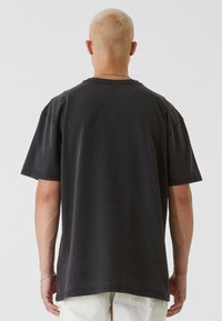 Čierne bavlnené tričko s uvoľneným strihom, krátkymi rukávmi a okrúhlym výstrihom, s opotrebovanou textúrou a surovými okrajmi na spodnom leme.