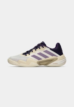 Sportliche Schuhe in Weiß und Beige mit lila Akzenten, ausgestattet mit einem strukturierten Mesh-Obermaterial und einer Gummisohle mit einem Zickzack-Profil.