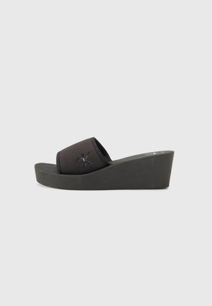 Black wedge sandals with a canvas upper featuring a logo. The sole is thick and made of a textured material for traction.