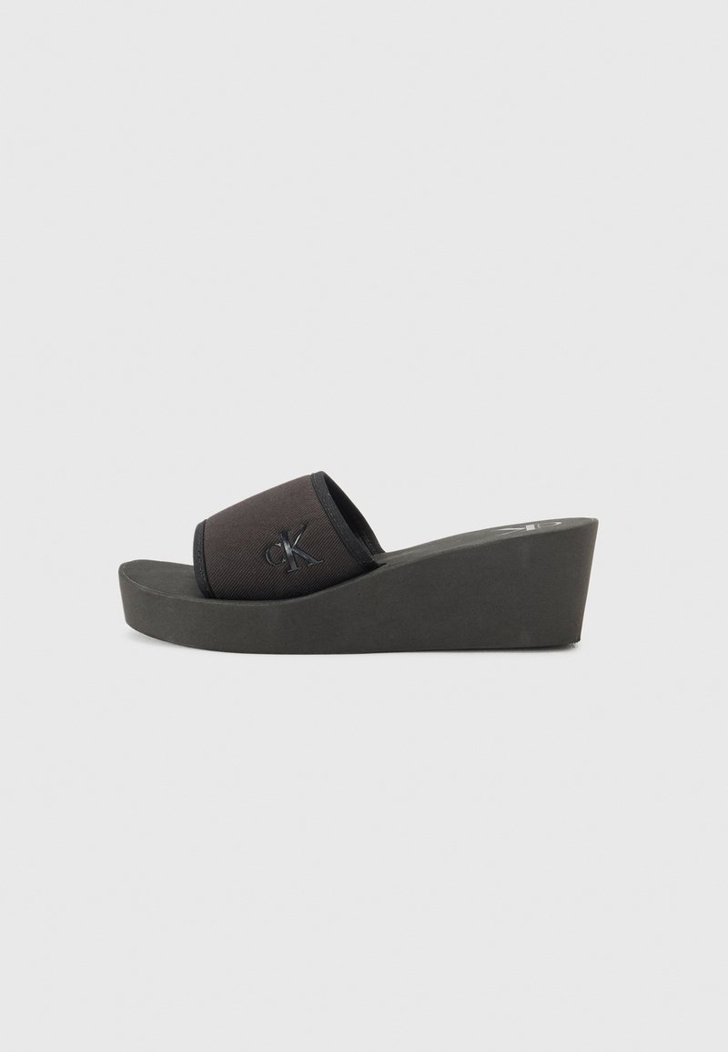 Sandale negre cu toc wedge, cu un superior din pânză care prezintă un logo. Talpa este groasă și realizată dintr-un material texturat pentru aderență.