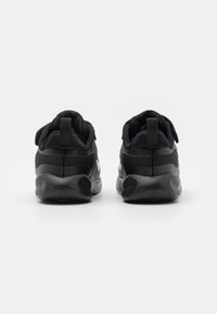Chaussures de sport noires en matériau texturé, avec un col rembourré, une semelle grise contrastante et un design épuré. La vue arrière met en évidence des languettes de traction.