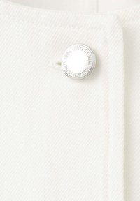 Tessuto denim bianco con un bottone d'argento inciso "ESTABLISHED 1984 ING DENIM" vicino a una cucitura.