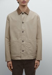 Beige jas gemaakt van gladde stof, met een bruine kraag, knopen aan de voorkant en twee opgestikte zakken. Eenvoudig design, standaard pasvorm.