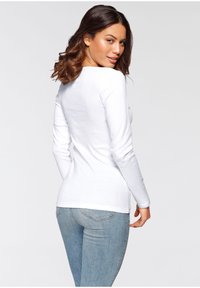Weißes Langarmshirt mit taillierter Passform, runden Halsausschnitt und glatter Textur, kombiniert mit hellblauen Denim-Jeans.