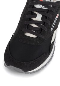 Pantofii sport negri au un superior din suede texturat, accente din plasă și detalii albe. Prezintă șireturi plate și o talpă din cauciuc pentru aderență.