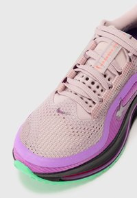 Baskets de sport violet clair avec une tige en mesh, semelle noire et verte, et accents violets. Présente un logo Nike violet sur le côté.