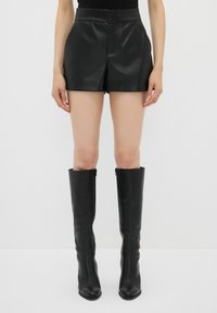 Pantaloni corti di pelle nera con vita alta, texture liscia e vestibilità su misura, abbinati a stivali neri al ginocchio dal design elegante.