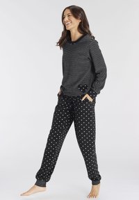 Black striped long-sleeve top with a heart pocket paired with black pants featuring small white heart patterns. Cuffed ankle design.