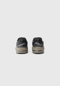 Mustad musta New Balance'i jalatsid hallide aktsentidega, võrgust ja sünteetilisest materjalist ülemine osa, pehme siseosa ja silmapaistva brändingu detail kandajal.
