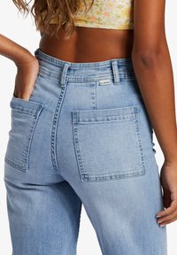 Light blue denim jeans with a high waist, two large back pockets, and visible stitching. The fabric appears soft and slightly textured.