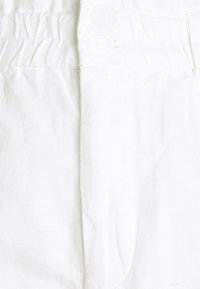 Tissu blanc à finition texturée, équipé de deux boutons blancs et d'un élastique froncé à la ceinture, créant une apparence lisse et ajustée.