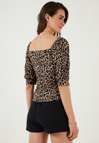 Blúzka s leopardím vzorom z ľahkej látky, s hranatým výstrihom a pufovanými rukávmi, v kombinácii s čiernymi šortkami.
