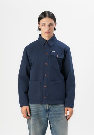 Navy blue jacket with a collar, front metal button closure, two large front pockets, and a small chest pocket with a label. Smooth fabric texture.