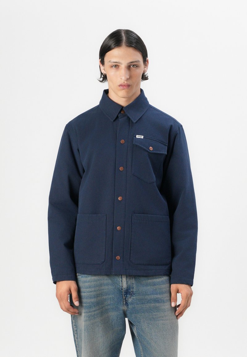 Navy blue jacket with a collar, front metal button closure, two large front pockets, and a small chest pocket with a label. Smooth fabric texture.