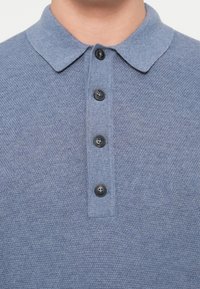 Strick-Polohemd in Hellblau mit strukturierter Stoffoberfläche, ausgestattet mit einem Kragen und sechs schwarzen Knöpfen auf der Vorderseite.