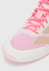 Athletic shoe featuring a pink mesh upper, white rubber sole, and tan accents. The design includes textured overlays and matching shoelaces.