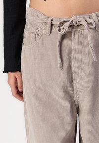 Pantalon en velours côtelé beige avec un motif texturé en côtes, doté d'une taille à lien de serrage et de deux poches avant.