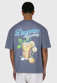 Grå T-shirt med korte ærmer, der prydes af et farverigt tryk af et glas lemonade med citroner, is og grønne blade på ryggen.