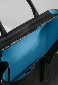 Czarna torebka wykonana z fakturowanego materiału, z niebieską podszewką, zamknięciem na zamek błyskawiczny oraz podwójnymi uchwytami do noszenia.