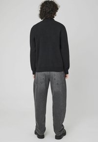 Un pull en tricot noir à col montant, associé à un pantalon en denim gris ajusté. Il présente des poignets côtelés et une texture lisse.