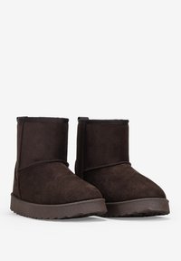Stivali alla caviglia in suede marrone con suola piatta in gomma, punta rotonda e dettagli di cucitura sottili lungo le cuciture. Design semplice senza decorazioni.