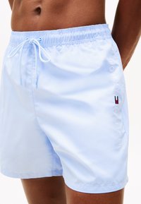 Shorts de bain bleu clair en tissu lisse. Dotés d'une taille élastique avec cordon de serrage et d'un logo brodé sur le côté.