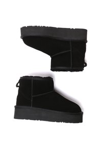 Black suede ankle boots with a flat rubber sole, featuring a shearling lining, stitching accents, and a pull tab at the back.