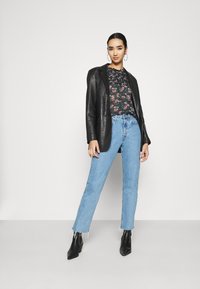 Blazer di pelle nera su una maglietta a fiori, abbinato a jeans azzurri con orli sfrangiati e stivaletti neri.