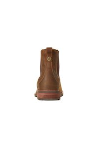 Stivaletti Chelsea in pelle marrone con pannelli elastici laterali, punta rotonda e tacco in stile legno. Presenta un piccolo accento dorato sulla linguetta del tacco.