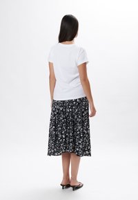 Hvid kortærmet t-shirt parret med en sort midi-nederdel med blomsterprint, der har et lagdelt design og en elastisk talje. Sorte slide sandaler.